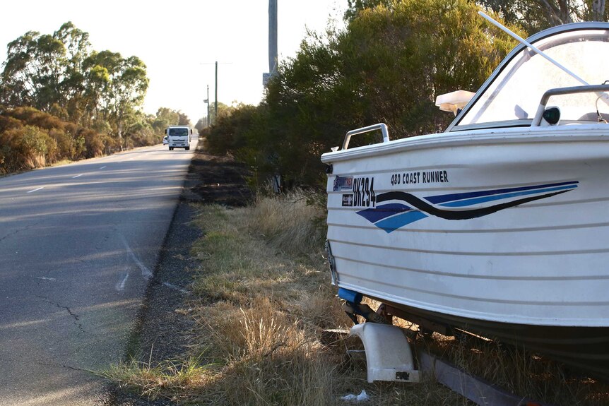 A boat on a trailer on the side of a bush road.