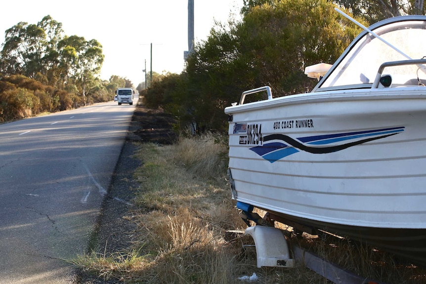 A boat on a trailer on the side of a bush road.