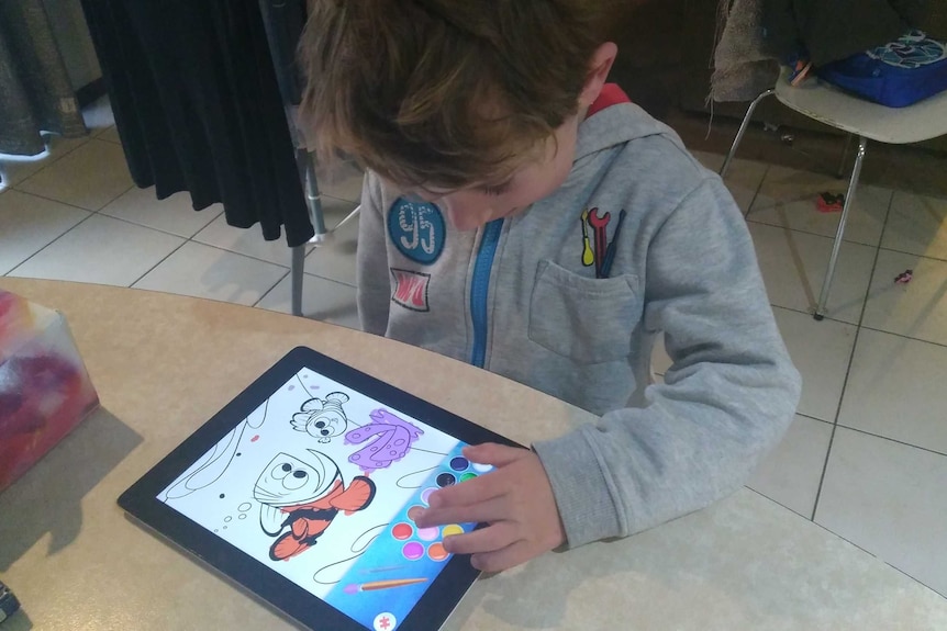 A five year old boy does a colouring activity on a tablet device.