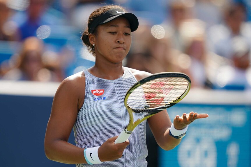 Naomi Osaka holds her racquet above her outstretched hand and grimaces