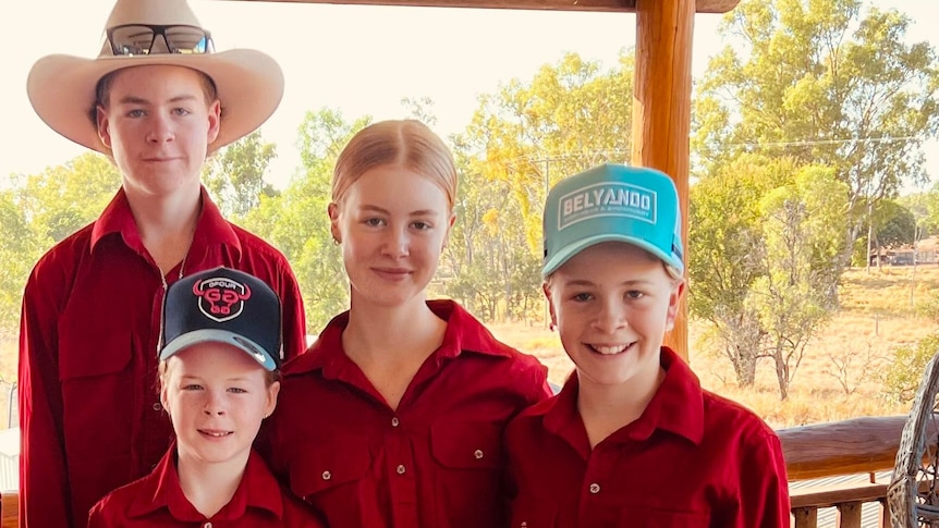 Four children stand in matching red shirts smiling at the camera. 
