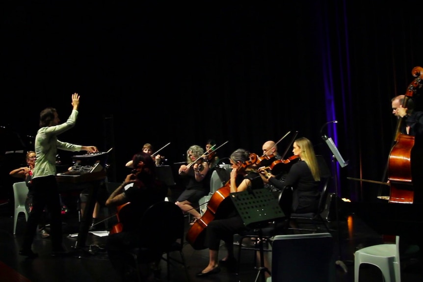 An orchestra performs on a black stage