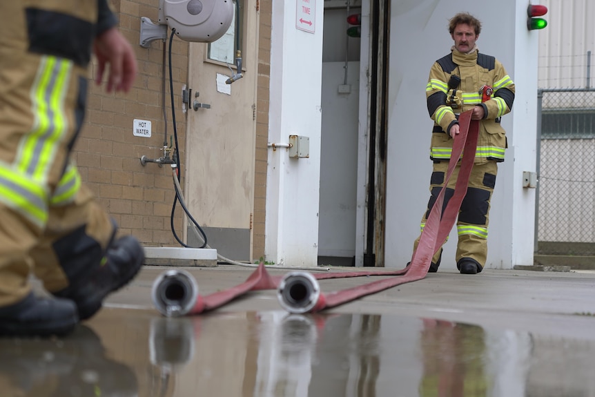 A firefighter unravels a firehose, the legs of another firefighter can also be seen holding other end