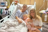 Two women and a toddler girl in a hospital room. One of the women lays in a hospital bed.