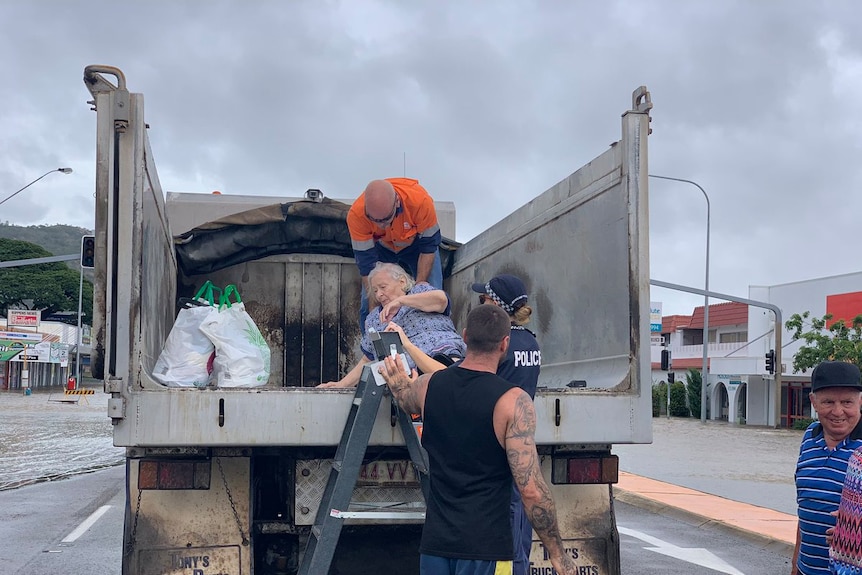 Authorities help an elderly woman onto the back of an empty truck during Townsville flooding crisis.