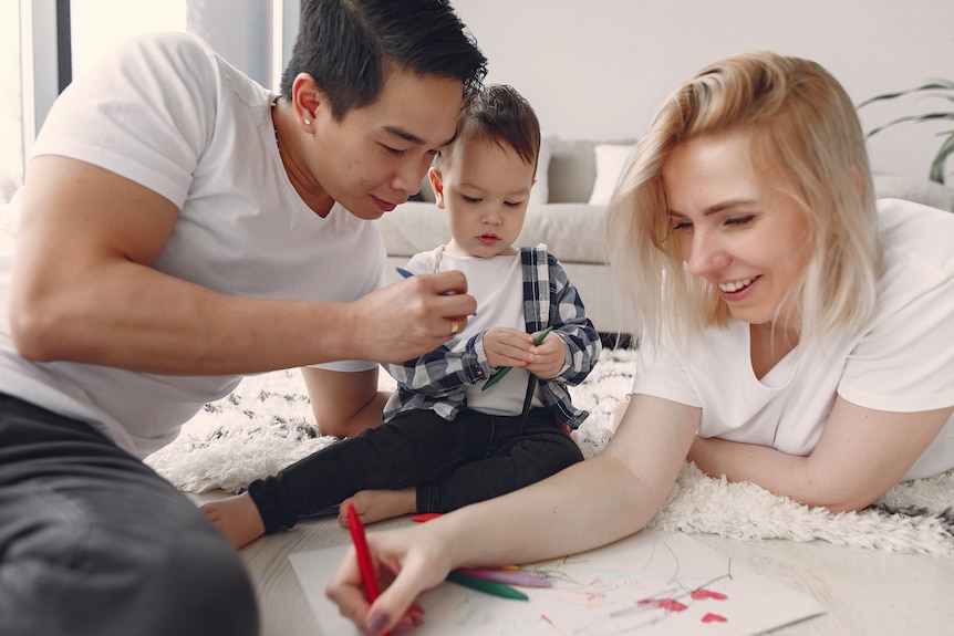 Two parents entertain their toddler with coloured pens, taking time to relax during the pandemic stress.