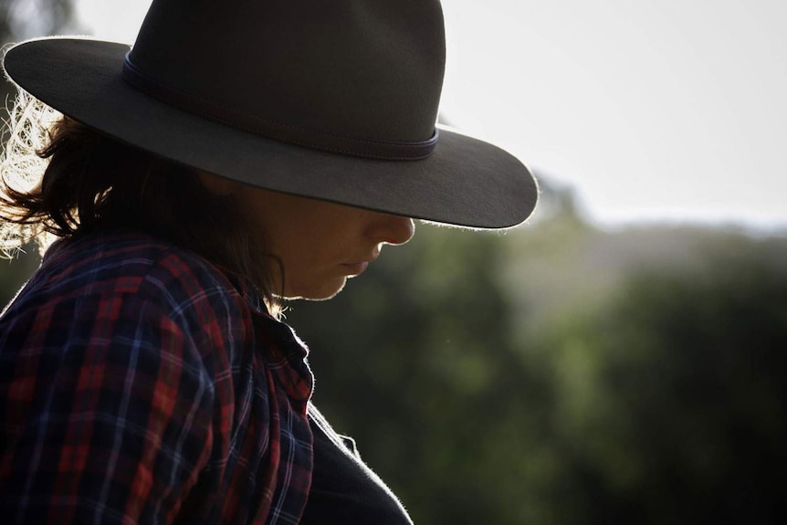Anonymous woman sits outside wearing an Akubra hat and checked shirt.