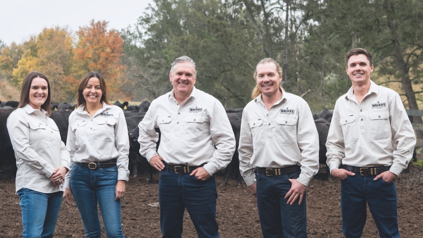 Two women and three men stand in a cattle yard smiling in khaki button-ups.