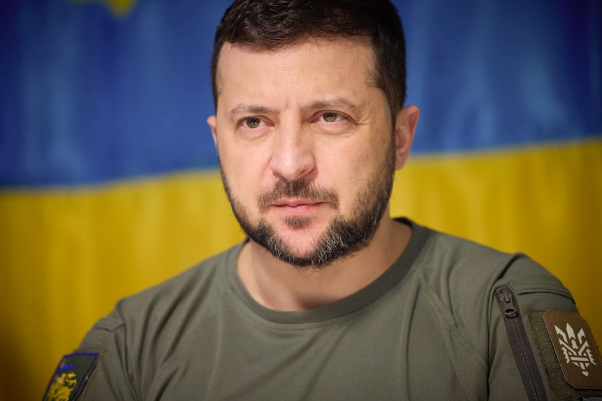A close up of Volodymyr Zelenskyy dressed in a green shirt and staring intently ahead.