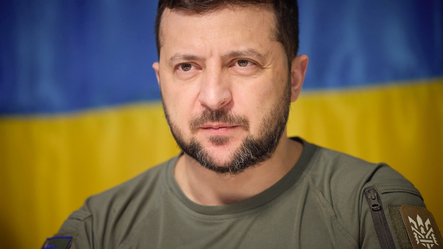 A close up of Volodymyr Zelenskyy dressed in a green shirt and staring intently ahead.