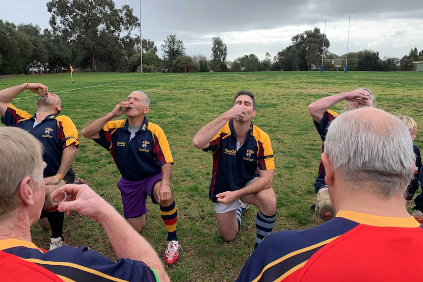 Senior rugby players kneel on the field to take a shot of port