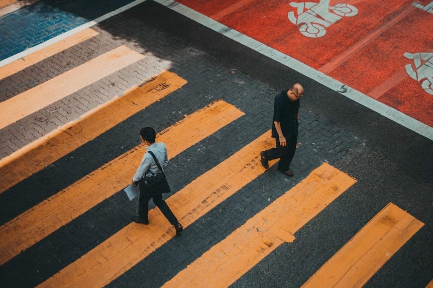 Yellow zebra crossing is seen as two men walk across it in opposite directions with their heads bowed.