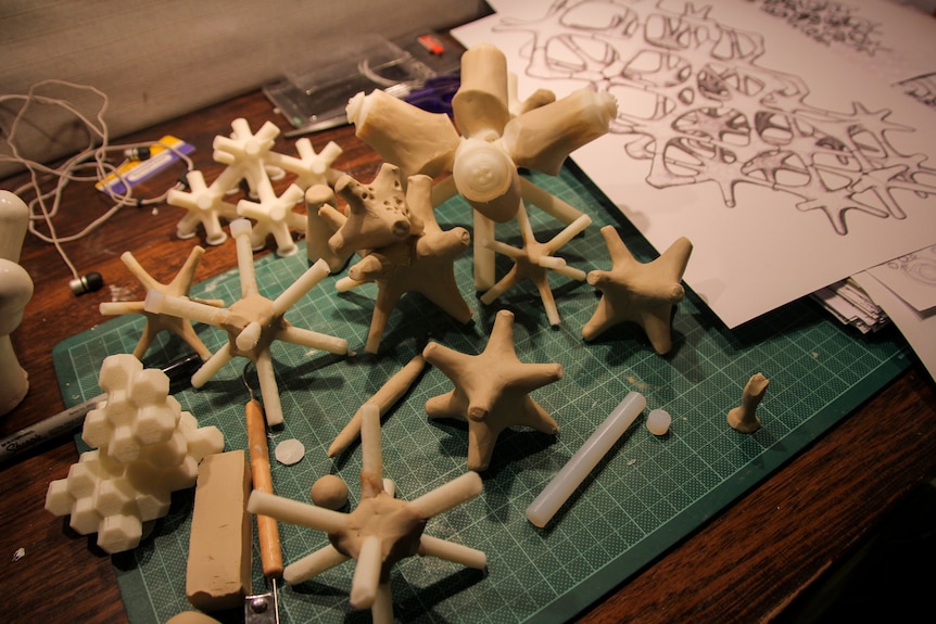 You look down at a desk strewn with prototypes of coral-like figures on a green cutting mat.