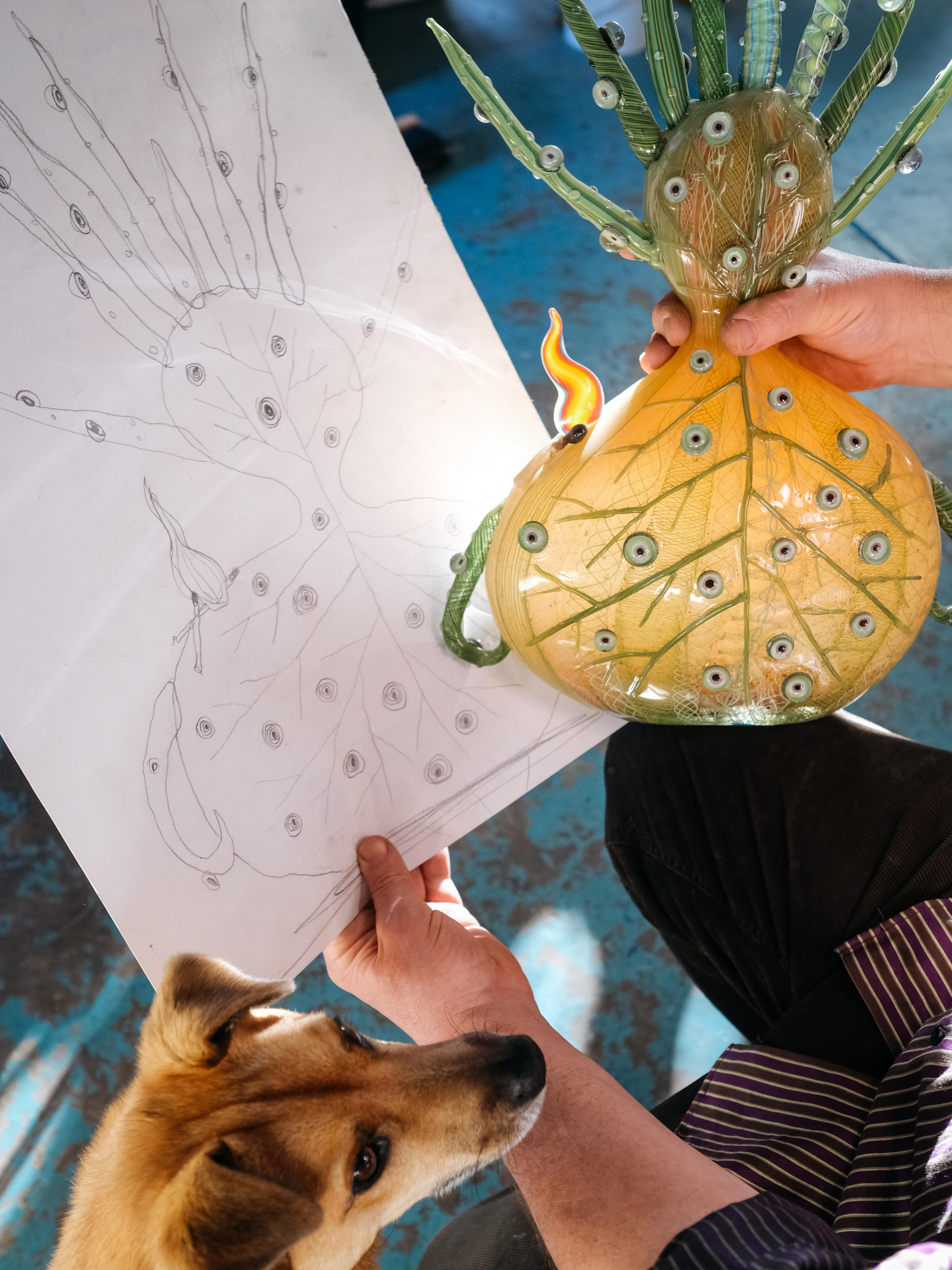 Close up on artist Tom Moore's hands holding a sculpture that looks like a yellow brain coloured in eyes!