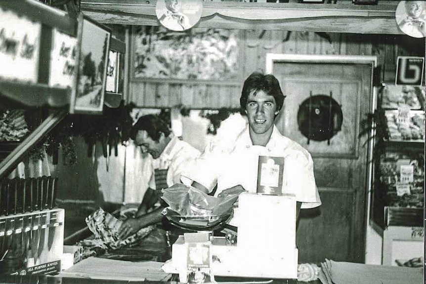 A black and white photo of a butcher weighing meat in a butcher's shop.