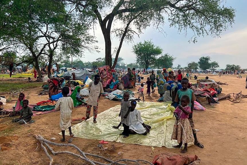 African family on a yellow tarp on dusty ground in countryside camp with tents behind