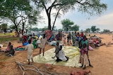 African family on a yellow tarp on dusty ground in countryside camp with tents behind