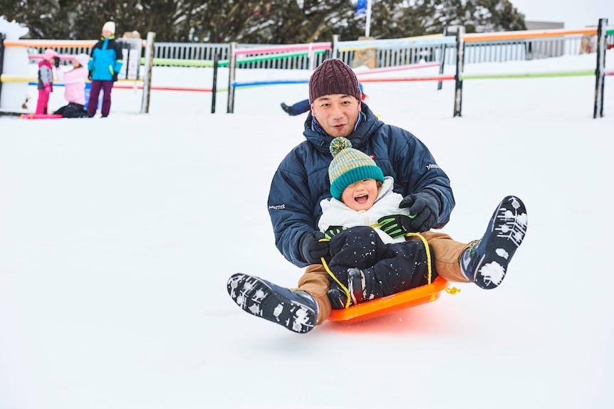 A father and children on a toboggan on Mt Buller