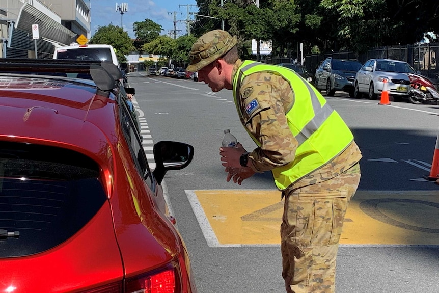 A Defence force member checking a vehicle and talking to the driver at a check point