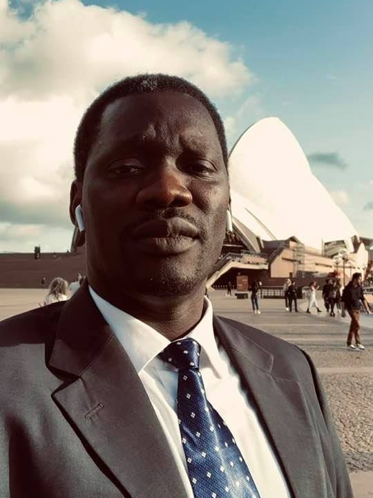 William Orule standing in front of the Sydney Opera House, wearing a suit.