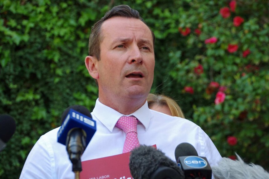 Mark McGowan talks to reporters with microphones in front of him.