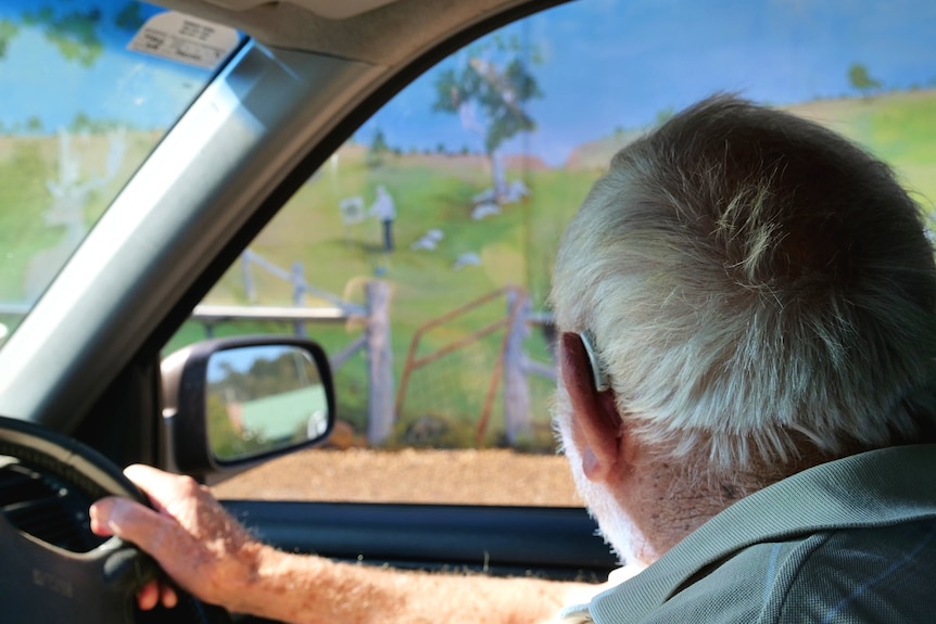 A man looks at a mural he painted from his car.