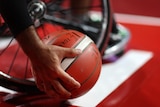 Wheelchair basketballer picks up the ball from down beside their chair during a match
