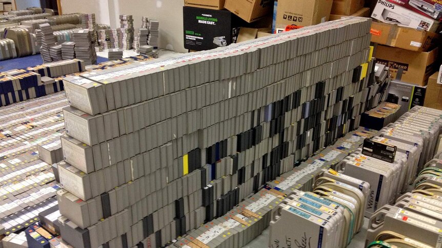 Hundreds of television video tapes in grey boxes stacked in an empty room.