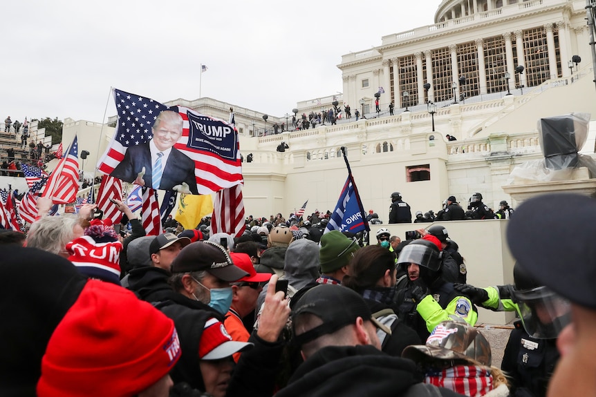 A crowd of people, waving US and Trump-themed flags, crushed together outside the Capitol building.