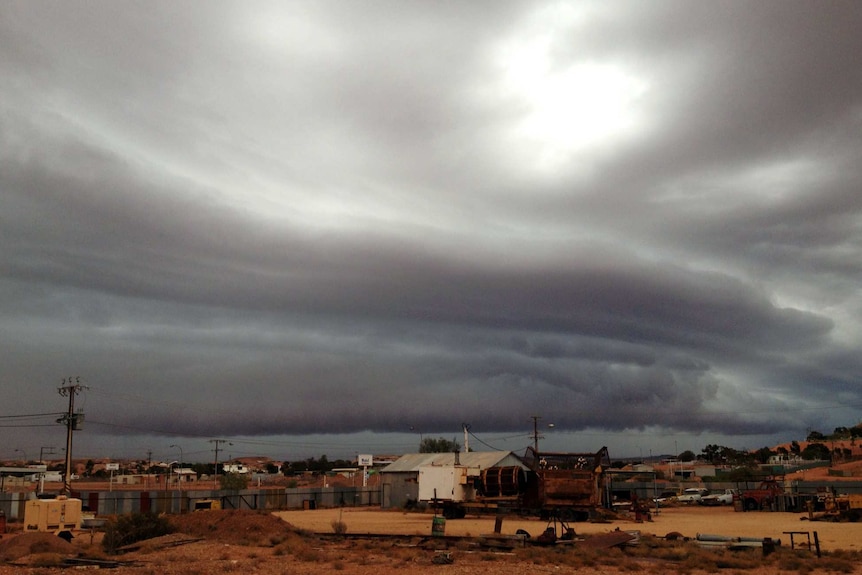 Low, dark storm clouds cover the sky over a ramshackle, dusty outback town
