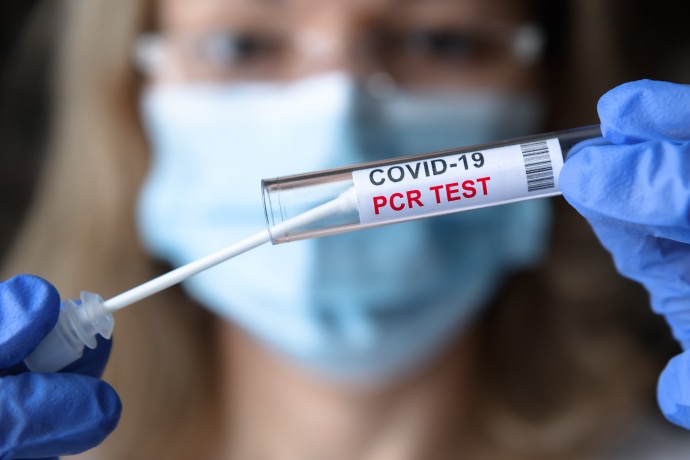 A woman in personal protective equipment holding up a COVID-19 polymerase chain reaction test