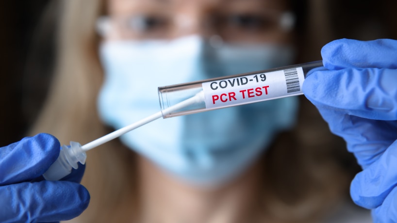 A woman in personal protective equipment holding up a COVID-19 polymerase chain reaction test