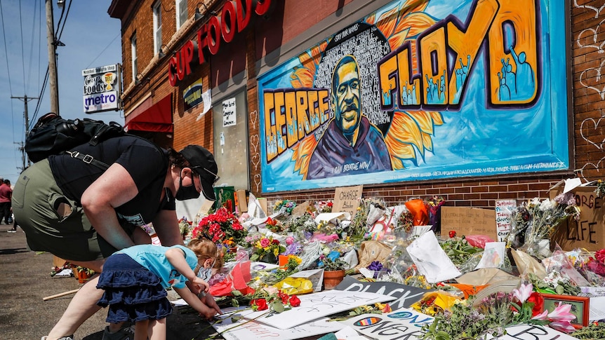 A woman and child add to a floral tribute in front of a mural of George Floyd