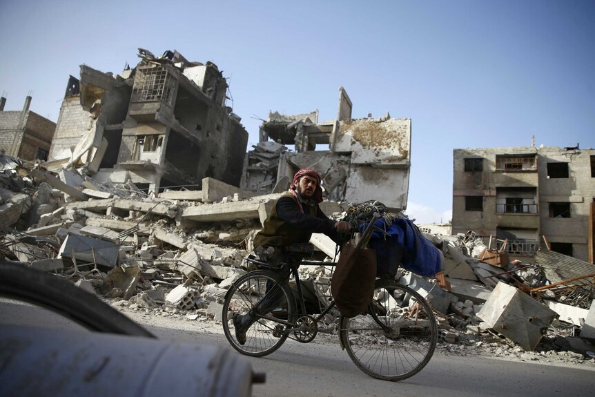 A handicapped man rides a bicycle past damaged buildings in Eastern Ghouta