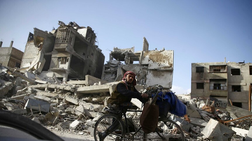 A handicapped man rides a bicycle past damaged buildings in Eastern Ghouta