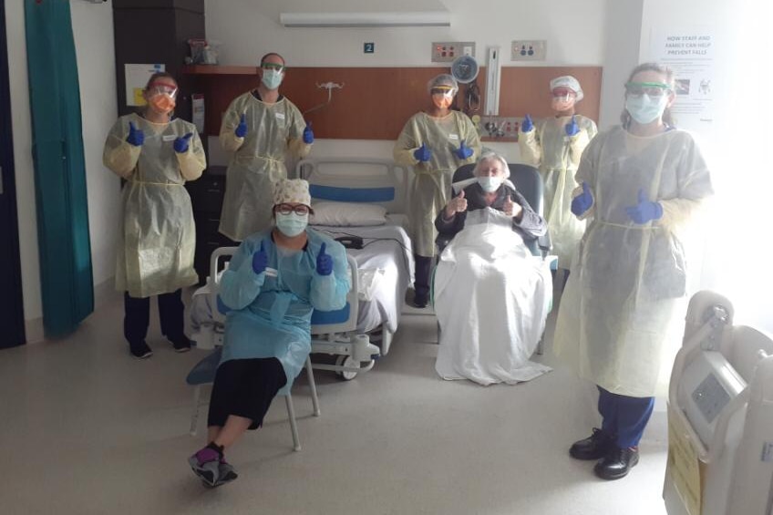 A patient and several staff in PPE give the thumbs up