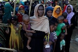 Rohingya refugee women queue for food aid, one woman holds a baby.