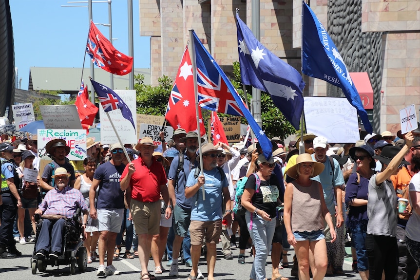 Lines of protesters walk along holding flags and placards.