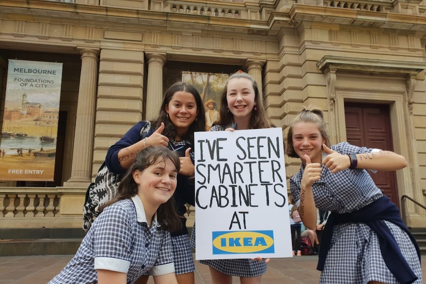 Schoolgirls hold a sign which reads: I've seen smarter cabinets at Ikea