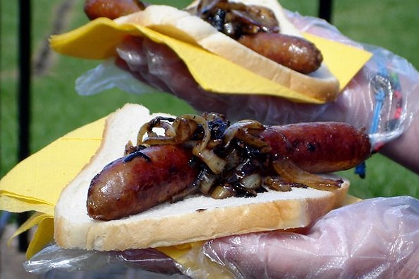 Two sausages in white break, both topped with onion and barbecue sauce.
