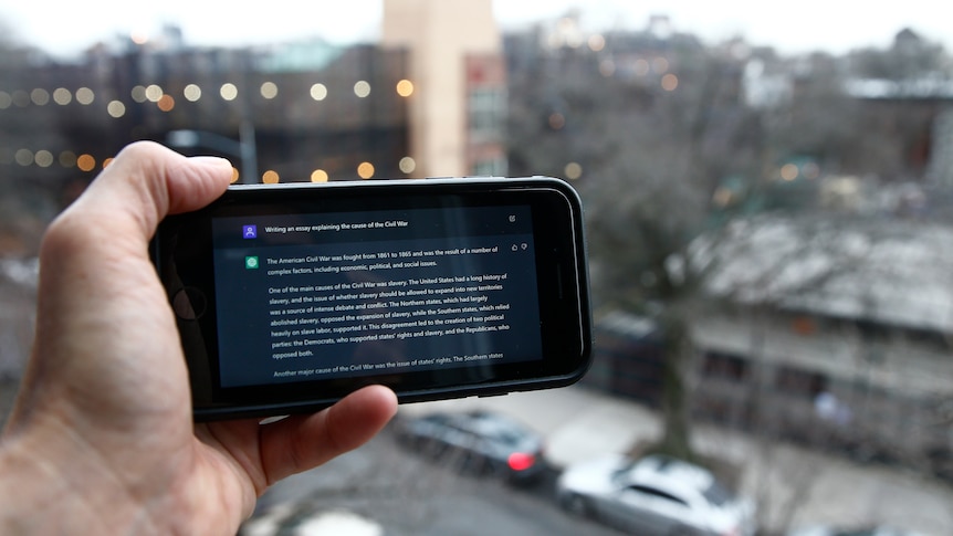 A hand holds a phone showing the ChatGPT prompt in front of a NYC view. 