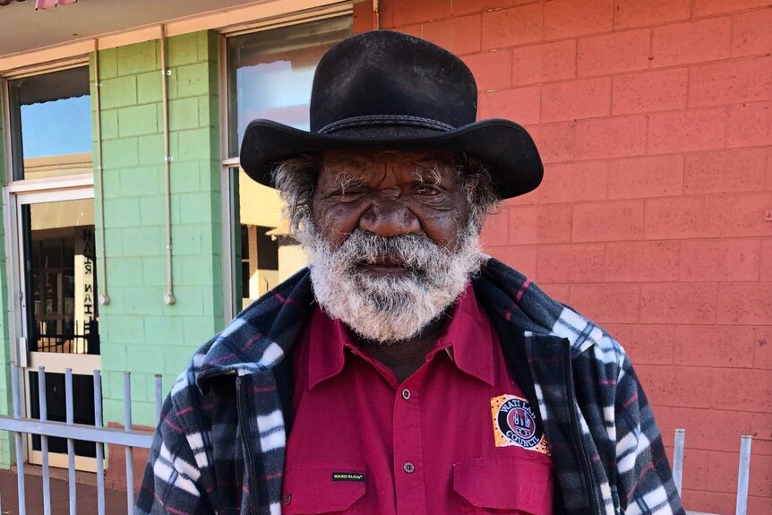 An elderly Indigenous man in a checked shirt and hat