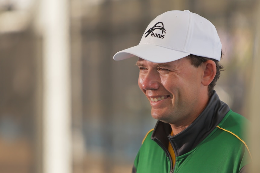 Archie Graham smiles wearing a green jacket and a white cap