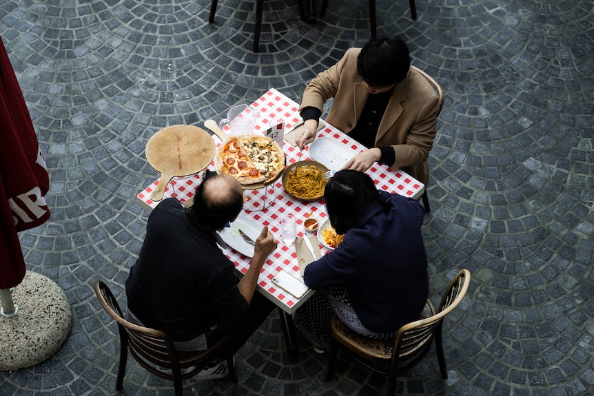 three people sit at an outdoor table eating food