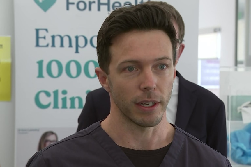 A close up of a man with short dark hair wearing medical scrubs