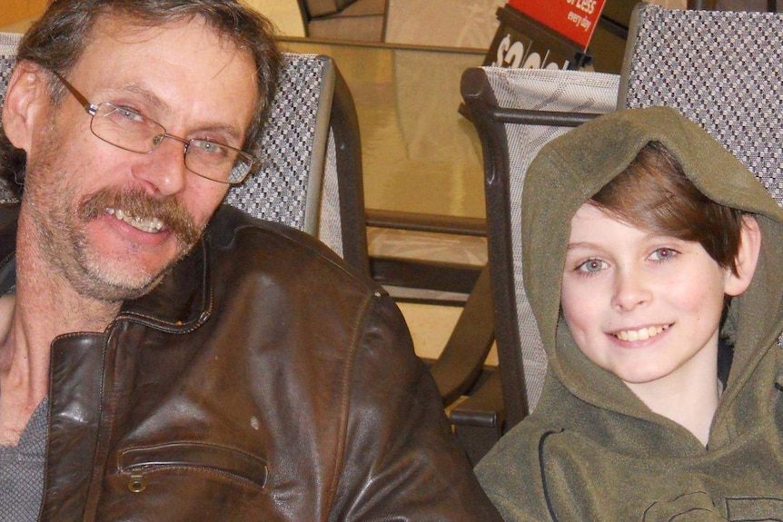 an older man and his son in a hoodie smiling at the camera