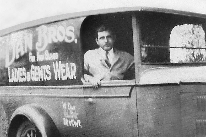 A black and white photo of a Lebanese man sitting in a Chevrolet, in 1929, with writing on the window advertising his business.