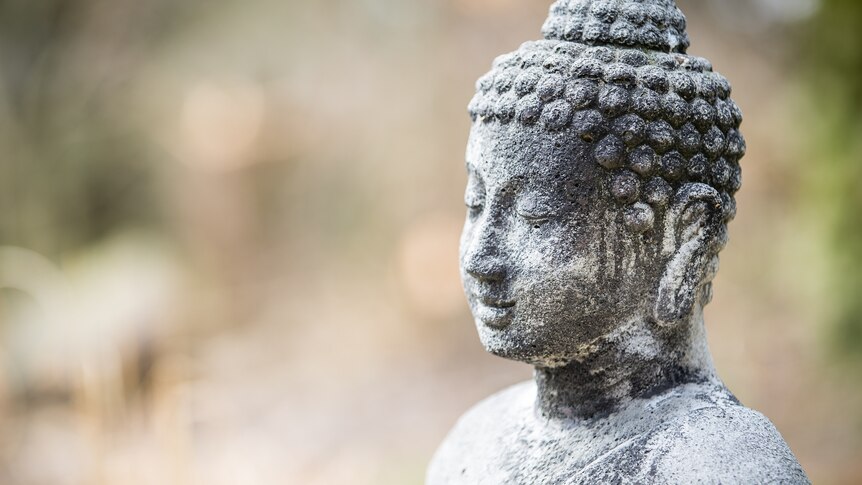 A stone buddha sits serenely in front of a blurred background.
