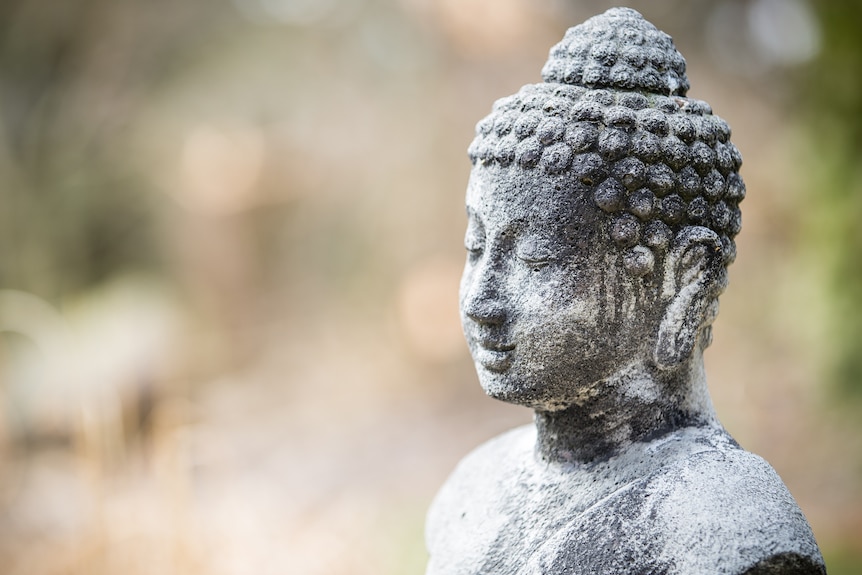 A stone buddha sits serenely in front of a blurred background.