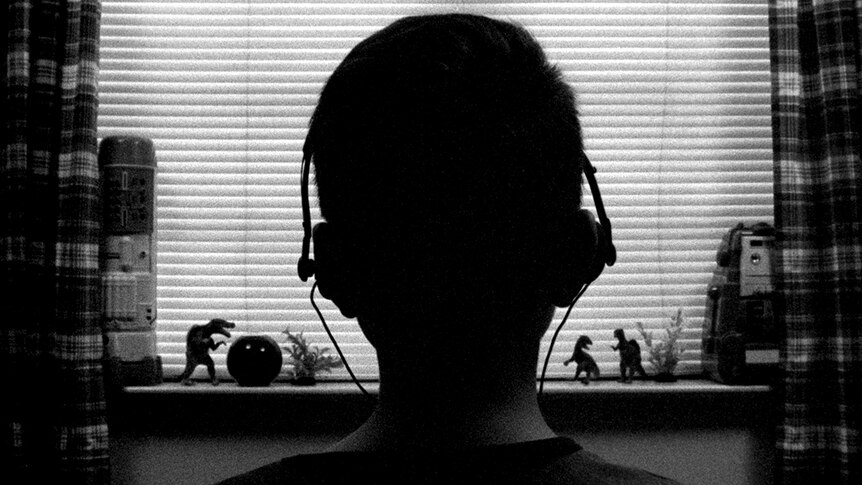 Black and white still of Aidan Langford wearing headphones with back to camera in front of bedroom window in 2018 film 1985.